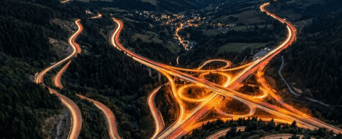 Aerial view of illuminated highway interchange with light trails in mountains at dusk